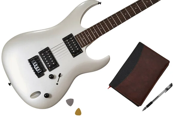 Bovenaanzicht van close-up van witte elektrische gitaar, twee bemiddelaars, close notebook en pen. Werkruimte van muzikant. Geïsoleerd op witte achtergrond met knippad — Stockfoto