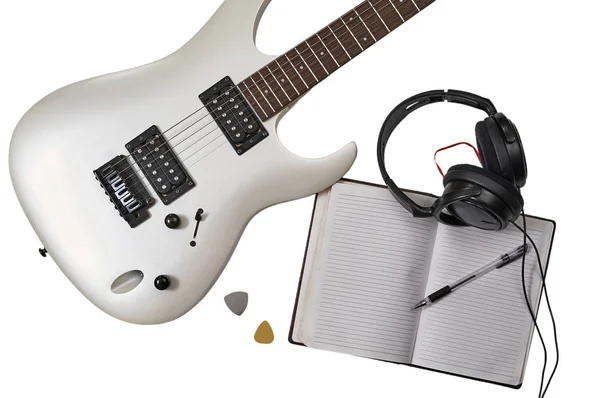 Bovenaanzicht van close-up van witte elektrische gitaar, twee bemiddelaars, open notebook, pen en hoofdtelefoon. Werkruimte van muzikant. Geïsoleerd op witte achtergrond met knippad — Stockfoto
