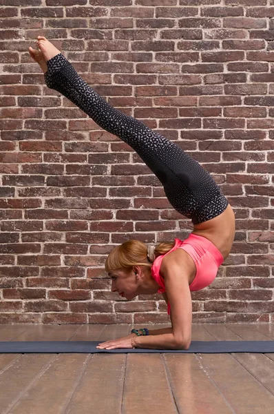 İnce vücutlu güzel bir kadın tuğla duvarda yoga yapıyor. 