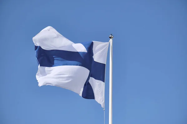 Vlag van Finland op een witte vlaggenmast tegen een blauwe lucht. — Stockfoto