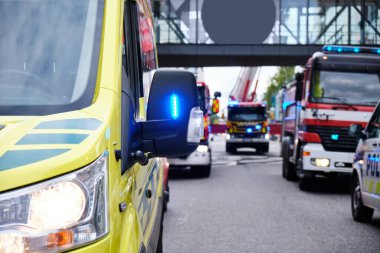 Ambulans arabası, itfaiye arabası ve alışveriş merkezinin yakınında mavi ışıklı bir polis arabası..