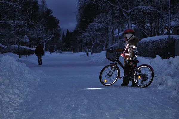 Girl on a bicycle in a winter evening. Light is reflected from clothing reflectors and bicycle wheels. Safe cycling in the dark time.