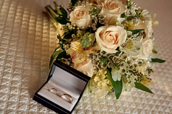 wedding bouquet and wedding rings sitting on a bed
