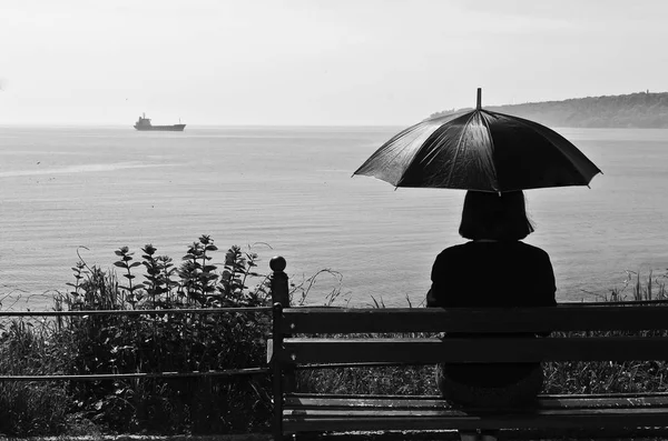 Silhueta de uma mulher em um banco olhando para o mar — Fotografia de Stock