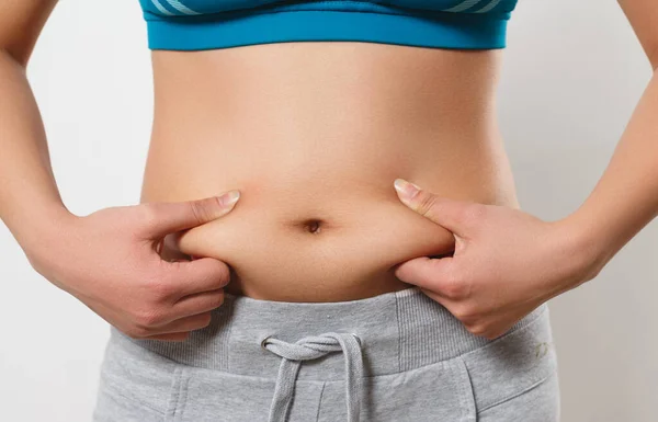 the woman presses her fingers to the folds of fat on the sides of her stomach