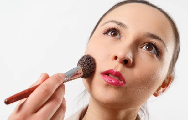 a young woman puts makeup on her face with a brush. on white background.