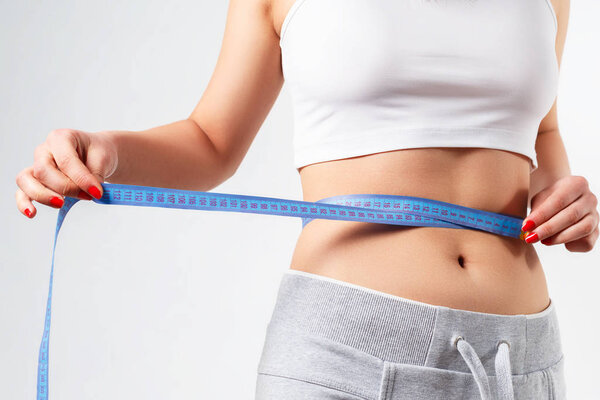 a young slender woman measures her waist with a centimeter tape. on white