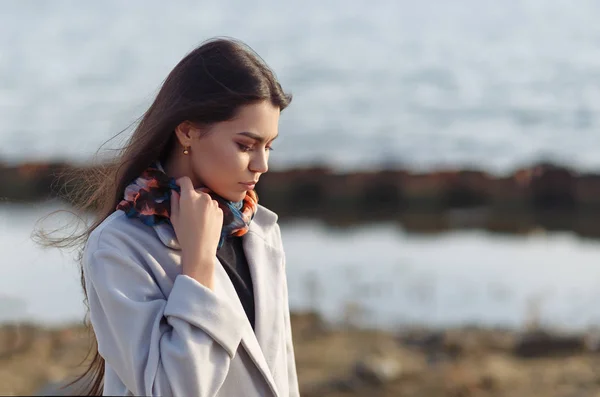 Portrait of a young beautiful charismatic brunette girl in a coat on the coast of the sea — 图库照片