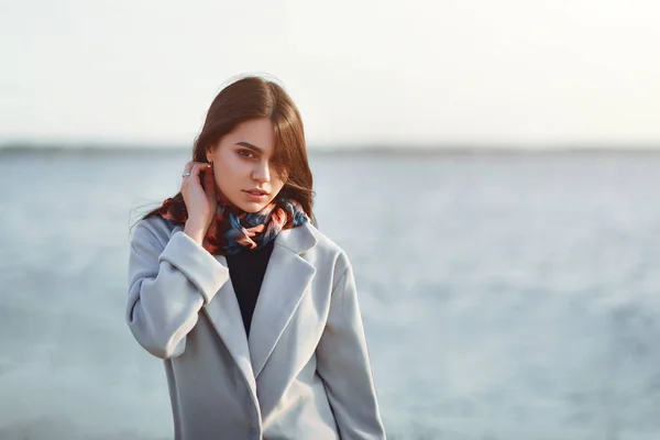 Portrait of a young beautiful charismatic brunette girl in a coat on the coast of the sea — 图库照片
