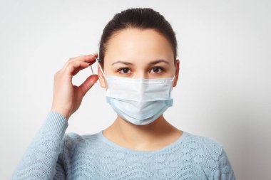 Studio portrait of young woman wearing a face mask, looking at camera, close up, isolated on gray background. Flu epidemic, dust allergy, protection against virus