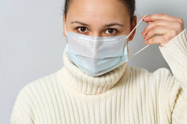 Studio portret van jonge vrouw met een gezichtsmasker, kijkend naar camera, close-up, geïsoleerd op grijze achtergrond. Griepepidemie, stofallergie, bescherming tegen virussen — Stockfoto