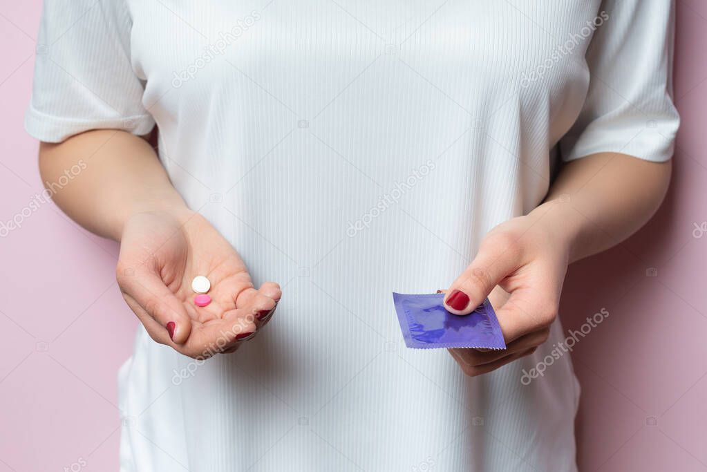 Contraceptive means: a condom and birth control pills in a hand on a pink background.