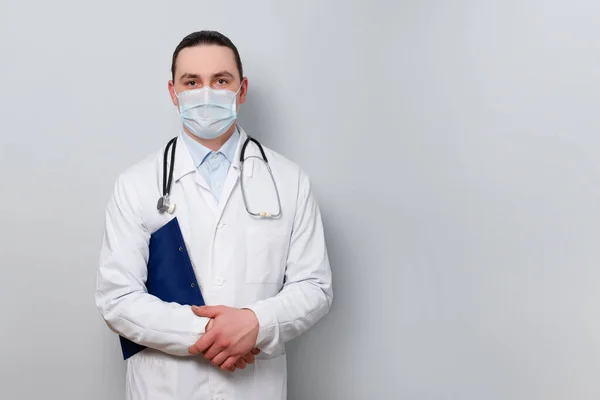 Elinde steteskop ve koruyucu bir maske takan genç bir erkek doktorun portresi. hafif arka planda. Yüksek çözünürlük Kopyalama alanı için yer