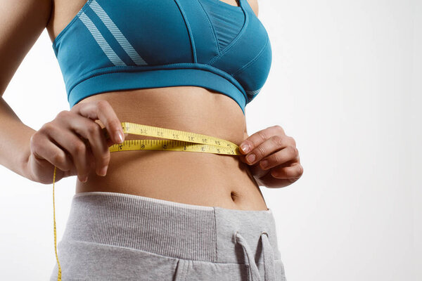 руки измеряют талию лентой. Подтянутая и здоровая женщина на белом фоне
