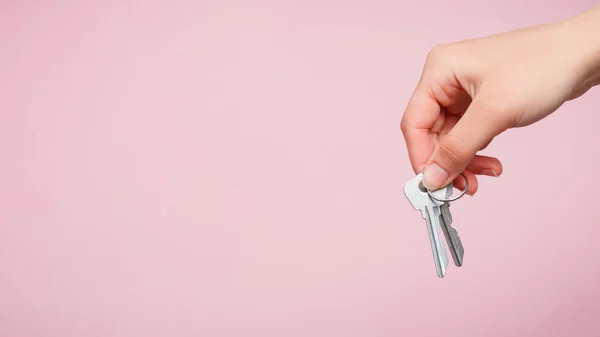 Bir kadının eli pembe arka planda iki anahtar tutar. kopyalama alanı için