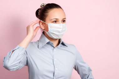 Yüz maskesi takan genç bir kadının stüdyo portresi, kameraya bakıyor, yakın plan, pembe arka plan izole edilmiş. Grip salgını, toz alerjisi, virüse karşı koruma. Şehir hava kirliliği kavramı