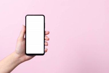 Akıllı telefonun kullanım konsepti. Elinde beyaz bir ekranı olan akıllı bir telefon bir kadının ellerinde. Pembe bir arka planda.