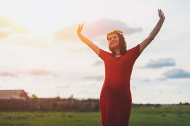 Genç, hamile, esmer bir kadın güneşli bir yaz akşamında dışarıda yürüyor. Hamilelik kavramı, çocuk beklemek..