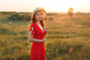 Gün batımında kırmızı elbiseli ve panama şapkalı güzel bir kızın portresi..