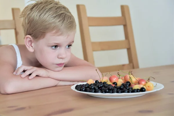 El niño está triste delante de un plato de bayas. alergia. enfermedad. pérdida de apetito . — Foto de Stock