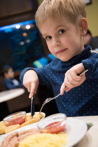 Estilo de vida. El niño está en el café con un cuchillo y un tenedor. El niño tiene pepitas. Aprende a usar un cuchillo y tenedor . — Foto de Stock