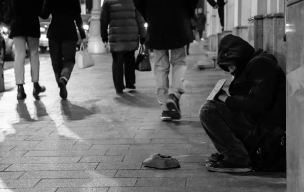 Een dakloze man zit op straat tegen de muur en vraagt om hulp.. — Stockfoto