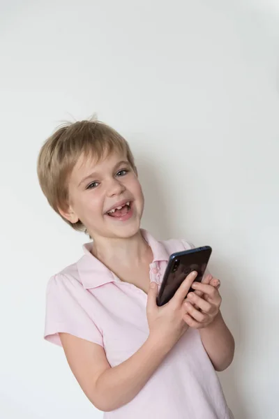 Un enfant mignon rit fort, tenant un téléphone portable dans sa main . — Photo