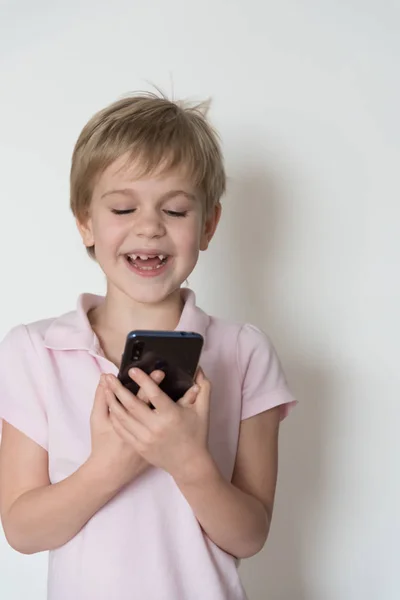 Un enfant mignon rit fort, tenant un téléphone portable dans sa main . — Photo