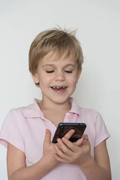 Un enfant mignon rit fort, tenant un téléphone portable dans sa main . — Photo
