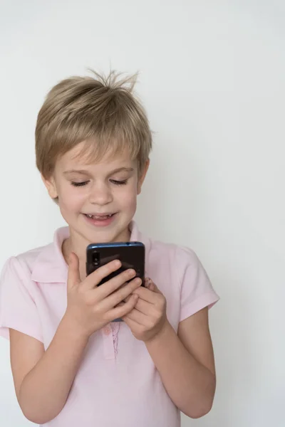 Un enfant mignon rit fort, tenant un téléphone portable dans sa main . — Photo