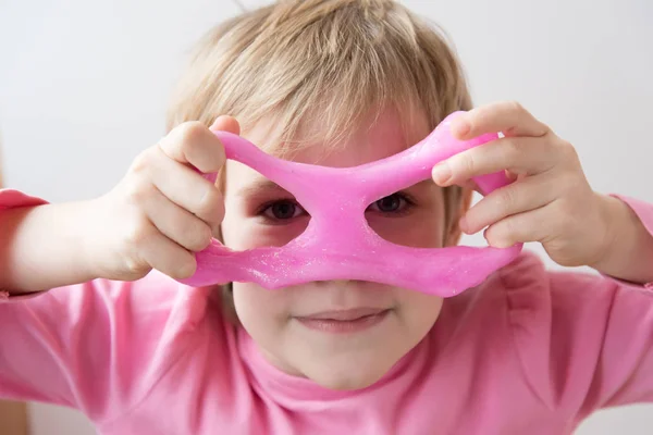 The child looks at the camera through slime glasses. Pink slime with sequins. Slime with your own hands. Concept. Pink glasses.