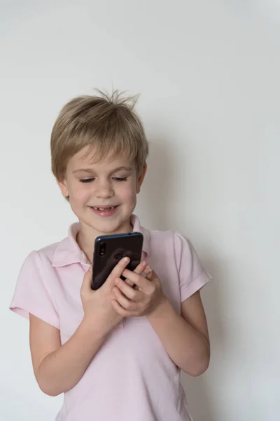 Un enfant mignon rit fort, tenant un téléphone portable dans sa main . — Photo