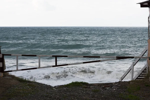 Die Straße zum Meer, die durch eine Barriere versperrt ist. Eine große Welle ist auf dem Meer zu sehen. Sturm. Konzept. — Stockfoto