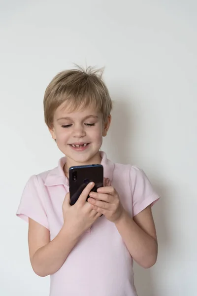 A cute child is laughing loudly, holding a cell phone in his hand. — Stock Photo, Image