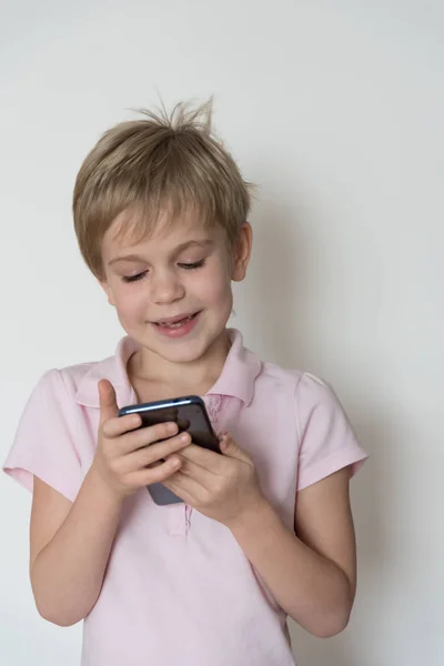 Un enfant mignon rit fort, tenant un téléphone portable dans sa main . — Photo