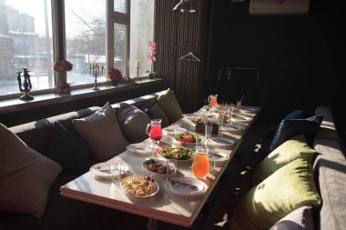 Küçük bir odada bir parti ya da ziyafet için masa hazırlamak. Masada tabaklar ve içecekler var ve yastıklı rahat koltuklar misafirleri bekliyor. Tavanın altında renkli balonlar.