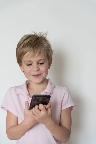 A cute little child looks at the phone screen and smiles sheepishly. — Stock Photo, Image