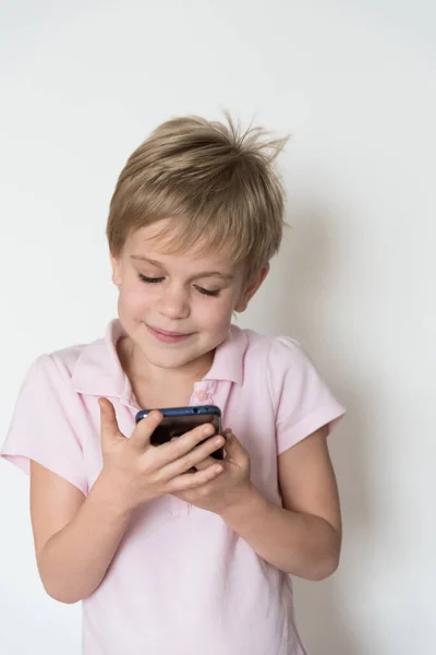 A cute little child looks at the phone screen and smiles sheepishly. — Stock Photo, Image