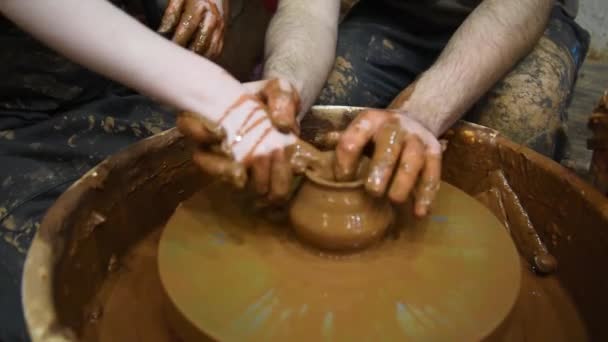 Töpferscheibe. Hinter dem Töpferrad arbeiten zwei Personen: ein Erwachsener und ein Kind. Ein Erwachsener bringt einem Kind Töpfern bei. Einen Tontopf machen. Konzept, Hilfe und Schulung. — Stockvideo