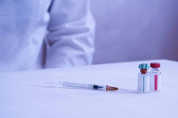 In front of the doctor on the table are vials of vaccine and a syringe. The doctor\'s hand is visible in a medical glove. Treatment of coronavirus. Vaccination against coronavirus. Prevention.