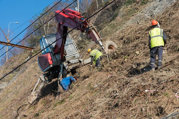 Los trabajadores fortalecen la ladera de la montaña con una malla metálica que evita caídas de rocas en la carretera. Equipo especializado se utiliza . — Foto de Stock