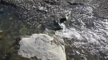 Bir dağ nehrinin berrak ve berrak sularında kayaların yakınına. Yukarıdan manzara. Kayalar aşağıdaki sudan görülebilir. Doğa sığ bir yol boyunca akar.
