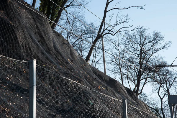 Fortalecimiento de la ladera de la montaña con una malla metálica que evita caídas de rocas en la carretera. Antecedentes abstractos del concepto de seguridad . — Foto de Stock