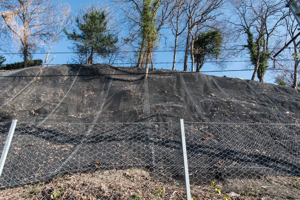 Fortalecimiento de la ladera de la montaña con una malla metálica que evita caídas de rocas en la carretera. Antecedentes abstractos del concepto de seguridad . — Foto de Stock