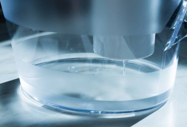 Su arıtma kartuşuyla bir sürahinin yakın çekimi. Fişekten bir su akışı akıyor. Arınma kavramı..