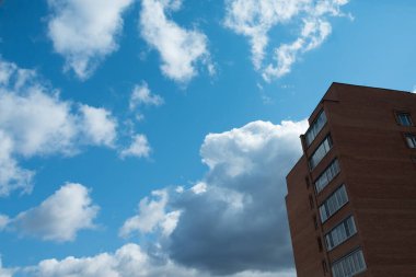 Parlak mavi gökyüzü ve beyaz bulutlar. Çok katlı bir binanın bir kısmı görülebilir. Metin için boşluk.
