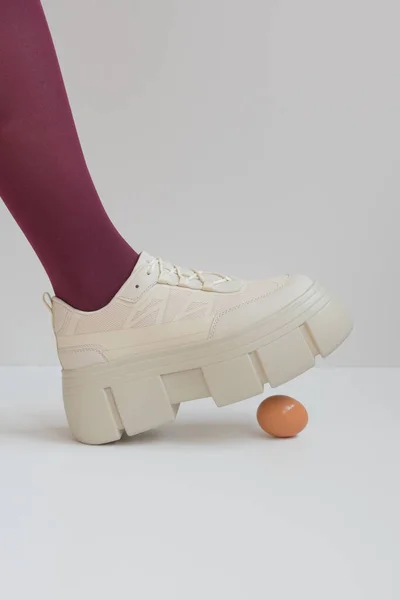 Het ei, waarboven een voet in de ruwe en massieve schoenen hing. Het begrip gevaar en verzekering. — Stockfoto