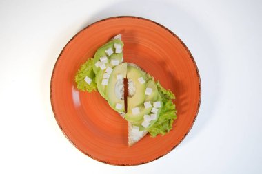 Turuncu tabakta yumuşak peynirli ve avokadolu sağlıklı bir sandviç var. Vejetaryenlik ve sağlıklı bir yaşam tarzı