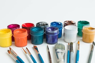 Kavanozlar dolusu guaj boyası farklı renklerde. Onun yanında çeşitli boyutlarda fırçalar var. Sanatçı çantası. Yan görüş. Beyaz arka plan. Hobiler