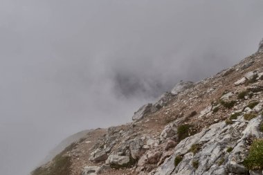 Gri havada uçurumun kenarında bulutlar alçaktan sarkmış.